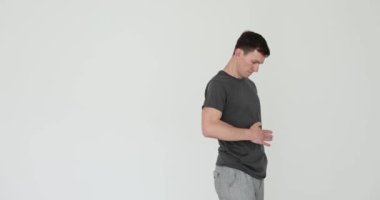 Rahatlamış bir adam, beyaz arka plandaki doyurucu öğle yemeğinden sonra karnına dokunur. Gülümseyen adam yemek yedikten sonra doymuş hissediyor. Ağır çekimde tatmin oluyor.