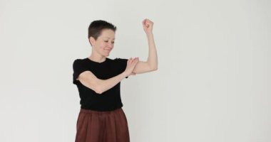 Pozitif kısa saçlı kadın beyaz arka planda kol kasları gösteriyor. Spor salonundaki başarısından gurur duyan sıradan giysili komik kadın. Sportif yaşam