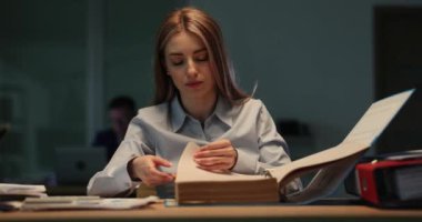 Genç kadın muhasebeci ofiste geç saatlere kadar çalışan mali belgeleri inceliyor. Yoğunlaşmış kadın evrak işleriyle uğraşıyor ve bilgiyi analiz ediyor.