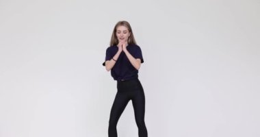 Sportif genç bir kadın beyaz duvarda aktif kalça egzersizi yapmaktan hoşlanıyor. Kendine güvenen bayan dans egzersizi yapıyor spor kulübündeki dinamik müziğin tadını çıkarıyor.