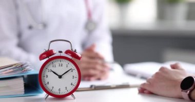 Doctor communicates with patient of clinic on table is alarm clock.