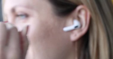 Smiling woman presses answer button on headphones in ear. Wireless trendy headphones concept