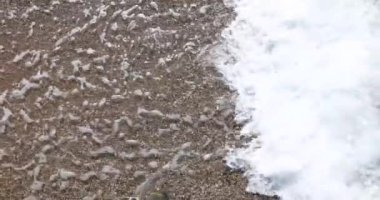 Yavaş çekim video beyaz köpük dalgası güneşli bir günde deniz kenarındaki çakıl taşlarında kıyıya vurur.