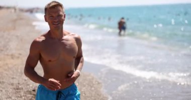 Gülümseyen yakışıklı adam sahilde deniz boyunca koşar. Yaz koşusu ve sağlık