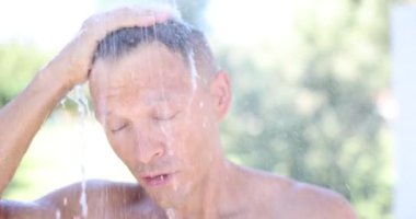 Tropik bahçede duş alan genç çekici bir adamın yakın plan portresi. Turistler için yaz tazeleyici duş