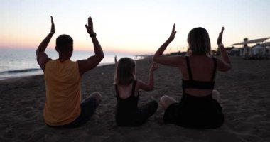 Baba ve kız gün batımında yoga yapıyorlar. Mutlu aile deniz kenarında yoga egzersizleri yapıyor.