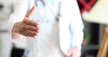 Tıp doktoru klinikte yakın çekimde el sıkışmayı teklif ediyor. Selamlar ve hoş geldin jestleri ve doktorun el sıkışması.