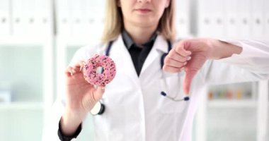 Diyetisyen kadın doktor elinde tatlı çörek ve elinde negatif bir işaret tutuyor. Cilt ve diş sağlığına verilen tatlıların zararları