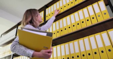 Muhasebeci üst raftan muhasebe malzemeleri için sarı klasör alıyor. Depolama ve iş belgeleri