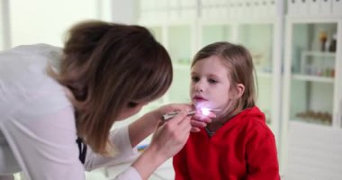 Kadın çocuk doktoru, çocuk kızın boğazına bakar. Doktor grip veya virüs enfeksiyonundan şüpheleniyor.