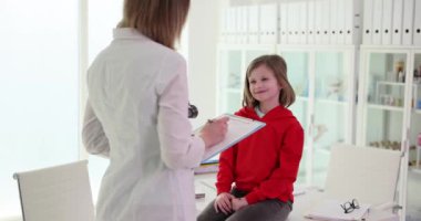 Klinikteki hasta çocukla konuşan ciddi bir kadın pediatrist. Doktor çocuğa sağlık ve şikayetleri soruyor.