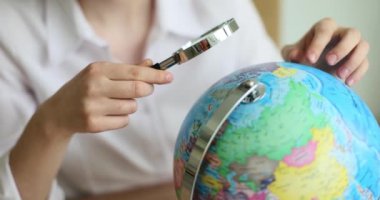 Turist büyüteçle dünya küresine bakıyor. Dünya turizmi ve egzotik yerler arayışı
