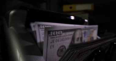 Karanlık arka planda nakit saymak için banka makinesine yakın çekim. 100 dolarlık banknotlar döviz ve makine para sayar.