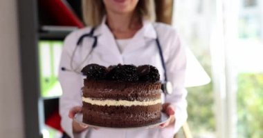 Beslenme uzmanı doktor elinde çikolatalı pasta tutuyor. Düzgün beslenme ve sağlığa zararlı tatlılar