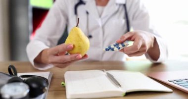 Doktor beslenme uzmanının elinde armut ve vitamin hapları var. Kozmetik uzmanı sağlıklı organik gıdaları vitaminlerle yemeyi tavsiye ediyor.