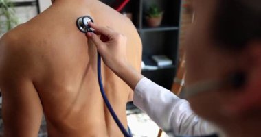 Terapist steteskopla nefes alan insanları dinler. Bronşit hastasının nefes alışını dinleyen bir terapist.