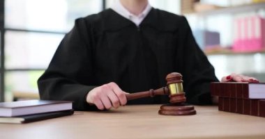 Kadın yargıç ahşap tokmakla kapıyı çalar ve kanun kitaplarının koleksiyonunda el ele tutuşur. Mahkeme ve adalet kavramı. Yargıç cüppeli kadın adaleti yönetiyor.