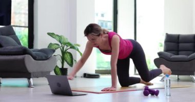 Kadın, dizüstü bilgisayara bakarak kol ve bacak egzersizi yapıyor. Evde eğitmenle fiziksel sağlık ve çevrimiçi ders verme kavramı