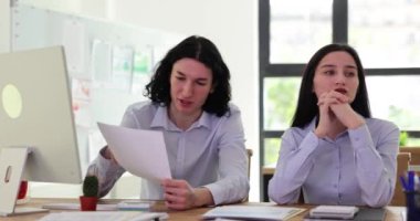 Ofis çalışanları kağıtları tartışır ve iş yerinde çözümleri değerlendirirler. Erkek müdür raporları yüksek sesle okur ve bayan meslektaşı düşünceli bir şekilde dinler.