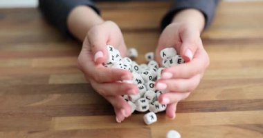 Kadın elleri ahşap masaya Latin alfabesiyle yazılmış büyük beyaz küpleri döker. Kompozisyon sözcükleri için harfleri olan plastik küpler