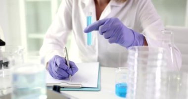 Bilimadamları test tüpü ve incelenmiş mavi reaksiyonla araştırma sonuçlarını tutuyorlar. Steril masada, manyetik karıştırıcıyla laboratuvar çalışanı ve kurusıkı tahta.