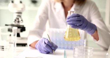 Kadın laboratuvar çalışanı, incelenmiş idrar örneğiyle birlikte araştırma sonuçlarını yazan bir şişe tutuyor. Steril klinikteki laboratuvar çalışanı tıbbi boşluğa veri yazıyor.