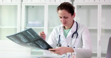 Hasta omurgasının röntgen görüntüsünü inceledikten sonra beyaz önlüklü genç bayan doktor tedavi için reçete yazıyor. Sırtında ciddi yaralar var. Sağlık tehlikesi