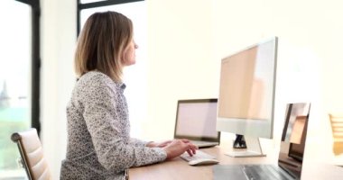 Kadın yönetici şirket ofisindeki bilgisayar üzerinde proje bilgileri. Bluzlu sarışın işçi ahşap masada dizüstü bilgisayarlarla oturuyor.