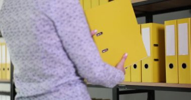 Kadın çalışan şirket arşivindeki raflara yüzük klasörü koymuş. Evrak ve belge depolama kavramları. Ofis işleri ağır çekimde.