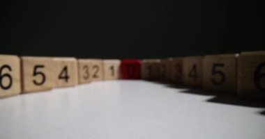 Wooden cubes with digits in descending order lead to red cube with zero. Lines of enumerated cubes stand on white surface against black wall in premise