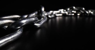 Massive silver chain links made of steel lies on black surface leaving bright reflection. Galvanized massive hard chains for different purposes put in dark studio