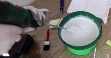 Builder stirs white paint in bucket with industrial mixer on floor in room slow motion. Worker prepares color material for house maintenance