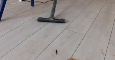 Cleaning parquet floor with domestic appliance in light room. Using vacuum cleaner for household chores. Routine housework with equipment