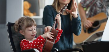 Portrait of mother take musical instrument from daughter hands to show how to play. Parent and daughter form home band. Music, creativity, talent concept clipart