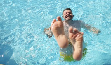 Portrait of man diving into water in swimming pool with feet up. Laughing cheerful middle aged male enjoy summer hot water. Summertime, fun, chill concept clipart