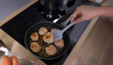 Köftelerin tavada kızarmaya başladığı mutfak sobası manzarası. Ev hanımı alet kullanarak taze yemek pişiriyor. Şef, yemek, yemek, yemek konsepti.
