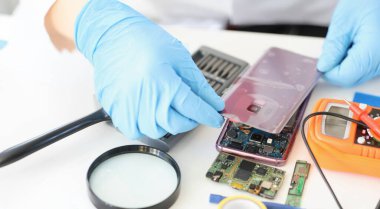 Erkek, cep telefonu kablosu bağlantılarına arka panel takmış. Eldivenli işçi modern cihazı tamir ediyor. Tamir servisi, hızlı yardım kavramı
