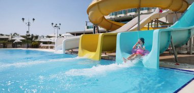 Su parkında pembe şiltede kayan mutlu küçük kız portresi. Gülümseyen çocuk yaz tatilinin tadını çıkarıyor. Yaz, tatil, eğlence konsepti