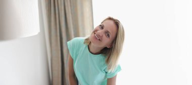 Mutlu gülümseyen sarışın genç bir kadının portresi. Dairede, perdede poz veriyor. Memlekette neşe dolu bir kadın. Modellik, rahatlama, ev hanımı konsepti