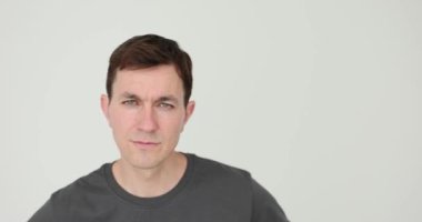 Mavi gözlü adam beyaz arka planda yavaş çekimde kameraya yaklaşıyor. Siyah tişörtlü ciddi bir adam yaklaşan bir şeye bakıyor.