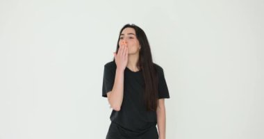 Uzun siyah saçlı genç bir kadın beyaz arka plana öpücük konduruyor. Bayan neşeli hareketlerle sevgisini ifade ederek mutluluk ve cazibe yayar.