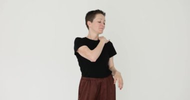 Gülümseyen kadın, beyaz arka planda duran omuzlarındaki tozu silkeliyor. Kısa saçlı kadın giysileri temizler. Toprağı temizler.