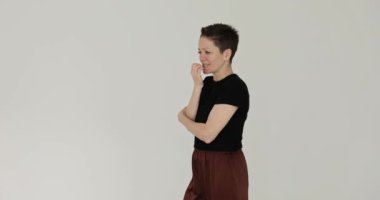 Kadın, beyaz arka planda yürürken tırnaklarını yiyor. Kısa saçlı esmer kadın kaygı ve gerginliğini mizahla ifade ediyor.