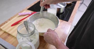 Erkek eller, mutfaktaki ahşap tezgahta metal kasedeki malzemeleri çırpıyor. Aşçı adam lezzetli krepler için hamur hazırlıyor.