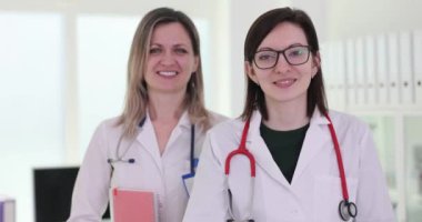 Kadın doktor, hastanede bayan meslektaşıyla baş parmak kaldırıyor. Kadın tıp çalışanları sağlık merkezinde pozitif enerji ve güven yayıyorlar.