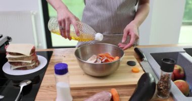 Önlüklü şef, ahşap tezgahta taze sebzeli zeytinyağı koyuyor. Yemekçi taze malzemelerle sağlıklı yemek hazırlar.