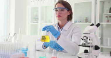 Kadın bilim adamı iş yerinde yağlı sıvı aromalı matara tutuyor. Kadın kimyager, laboratuarda yapılan deneylerden sonra aromanın aromasını inceliyor.