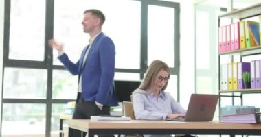 Yönetici, ofiste dizüstü bilgisayarla çalışan çalışanlara görevi açıklıyor. Profesyonel ofis ortamında iletişim ve rehberliği vurguluyor