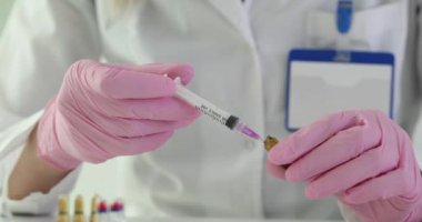 Pembe eldivenli hemşire şırıngayı hastane ofisindeki şişeden alınan sıvı ilaçla dolduruyor. Tıp işçisi ilaç işlemleri için aşı araştırması yapıyor.