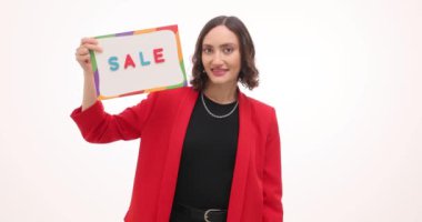 Kırmızı ceketli kadın kartonda indirimli tabela ve beyaz arka planda alışveriş torbaları gösteriyor. Sezonluk indirimden heyecanlanan gülümseyen bayan perakende satışları teşvik ediyor